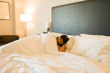 Sakin, iri yarı bir kadın, bir otel odasında rahat bir uyku çekiyor, uyku maskesi takıyor ve tatilinin rahatlığını ve rahatlığını kucaklıyor.