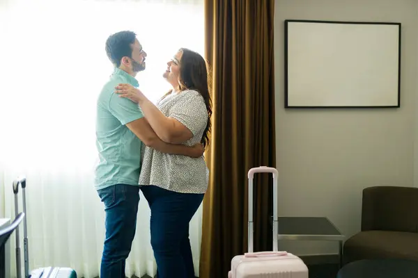 stock image Couple hugging in a warm hotel room. Surrounded by suitcases. Excited for a romantic getaway. Love and affection permeate the room as they embrace by the window. Making unforgettable memories together