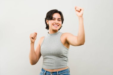 Tarafsız bir arkaplana karşı kazanılan zaferi kutlamak için kollarını kaldıran mutlu genç İspanyol kadın.