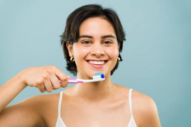 Dişlerini fırçalarken gülümseyen yirmili yaşlardaki bir kadın sağlıklı diş alışkanlıklarını teşvik ediyor ve ışıl ışıl gülümsüyor.