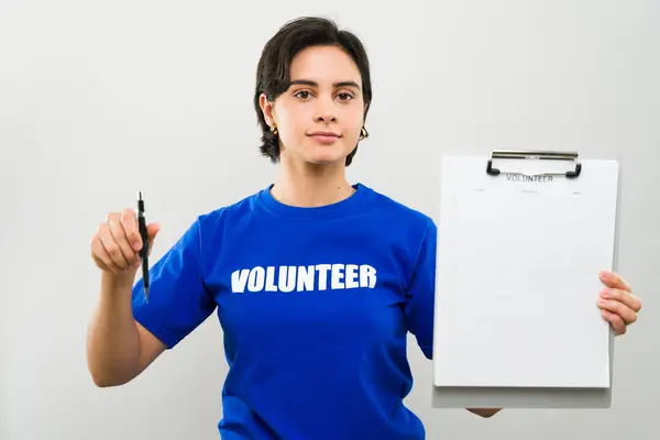 stock image Cute woman wearing a blue volunteer t-shirt is holding a clipboard and a pen asking people to join her cause