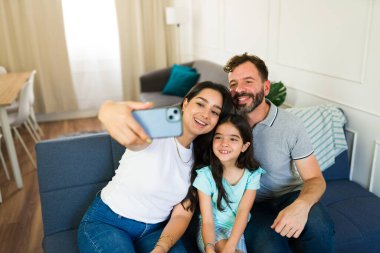 Oturma odalarında rahat bir kanepede otururken selfie çeken gülümseyen bir aile.