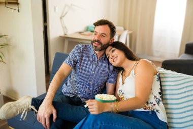 Mutlu çift kanepede gevşeyip, patlamış mısır yiyor ve film seyrediyor.