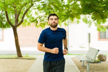 Genç atletik adam parkta spor giyerek koşuyor ve formda ve sağlıklı görünüyor.