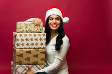 Noel Baba şapkası takan güzel bir genç kadın elinde bir yığın hediyeyle gülümsüyor ve kırmızı bir arka plana bakıyordu.