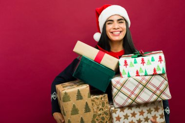 Mutlu genç kadın, kırmızı arka planda renkli kağıda sarılı bir sürü Noel hediyesi taşıyor.
