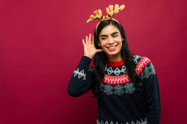 Ren geyiği boynuzu takan genç bir kadın Noel zamanı dikkatlice bir şeyler dinlerken gülümsüyor.