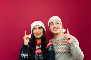 Stüdyonun arka planında Noel süveteri ve Noel Baba şapkası giyen genç İspanyol bir adam ve kadın.