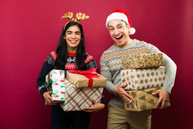 Neşeli ve genç çift canlı kırmızı bir zemin üzerinde sayısız Noel hediyeleri tutuyorlar.