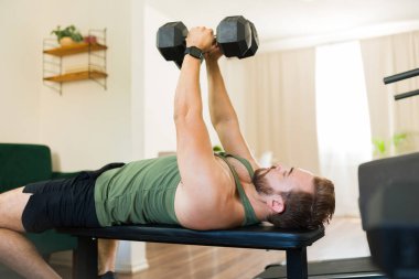 Genç sporcu spor salonunda çalışıyor ve ağırlık kaldırırken bir bankta yatıyor.