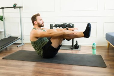 Konsantre olmuş bir adam, kişisel çalışma alanında yoga minderi üzerinde vücut egzersizi yaparken çevrimiçi fitness rutinini takip ediyor.