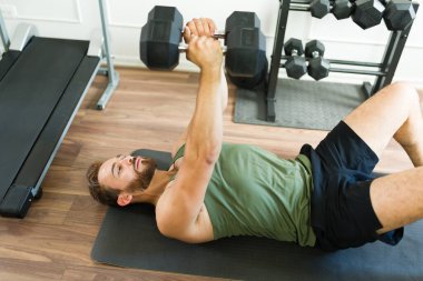 Formda genç bir adam spor salonunda spor yaparken egzersiz paspasına uzanıyor ve ağırlık kaldırıyor.