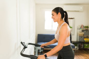 Spor kıyafetli genç bir kadın koşu bandında koşuyor ve gülümsüyor. Egzersiz yapıyor.