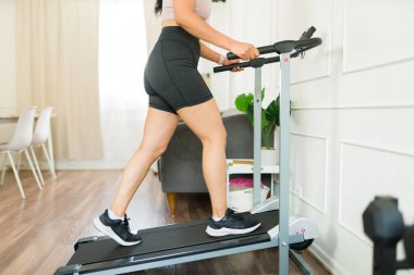 Atletik kadın koşu bandında yürüyor ve fiziksel durumunu iyileştirmek için evde egzersiz yapıyor.