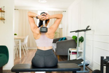 Güçlü bir kadın evinde ağırlık kaldırırken halterini kaldırıyor.