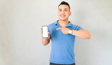 Stüdyoda dikilip onu işaret ederken boş ekranlı akıllı telefonu gösteren gülümseyen adam.