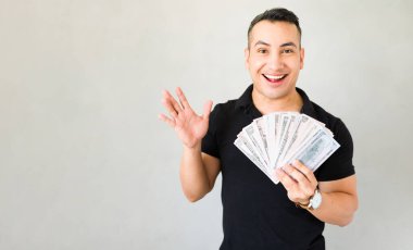 30 'lu yaşlardaki bir adam, elinde bir dolar fanı tutarak, gri bir arkaplana karşı stüdyoya ışınlanıyor, refah ve neşeyi temsil ediyor.