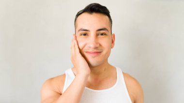 Genç adam nazikçe yüzüne dokunuyor. Stüdyo ortamında neşeli bir ifadeyle.