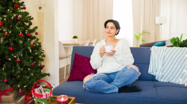 Huzurlu genç bayan, evdeki kanepede dinlenirken sıcak bir içkinin tadını çıkarıyor.