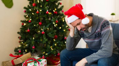 Evde Noel Baba şapkası takan bir adam üzgün ve hayal kırıklığına uğramış görünüyor.