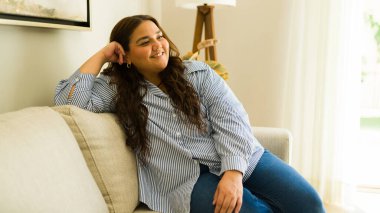 Genç ve cüsseli bir kadın oturma odasında rahat bir koltukta oturuyor. Huzur ve sessizliğin tadını çıkarıyor.