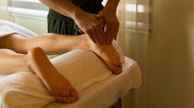 Masaj terapistinin masaj masasında yatan bir adama ayak masajı yapması.