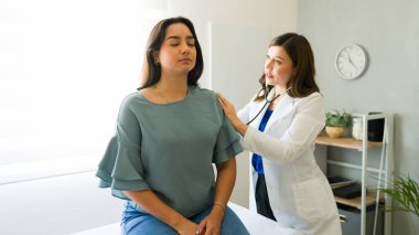 Tıbbi konsültasyon sırasında kadın bir doktor hastasının nefesini dikkatle dinler.
