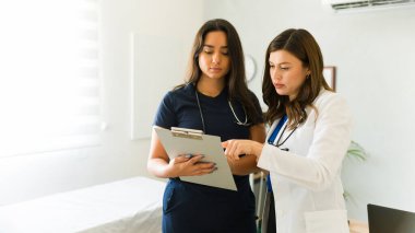 İki kadın tıp uzmanı bir doktorun ofisindeki panoya bakarken tartışıyorlar.