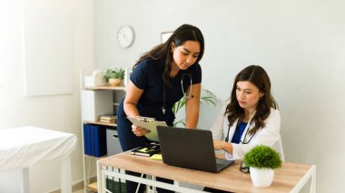 Kadın doktor ve hemşire iş birliği yapıyor, hasta bilgilerini laptopta analiz ediyor ve tedavi planlarını muayenehanede tartışıyorlar.