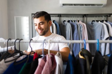 Genç adam, kıyafetlerini kendi dolabından seçiyor. Gömlek, pantolon ve ceketlerin arasından bakıp en uygun kıyafeti dikerken sırıtıyor.