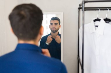 Yakışıklı adam, modern gömme dolabındaki aynaya bakarken gömleğinin düğmelerini ilikliyor.