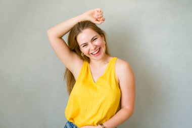 Genç bir kadın stüdyoda poz verirken gülüyor ve kolunu başının üstünde tutuyor.