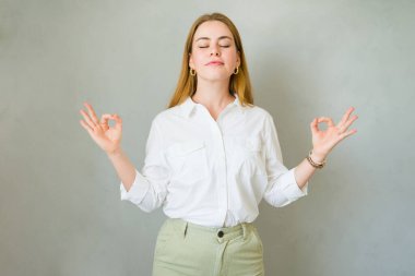Genç bir kadın elleri stüdyoda jest yaparken gözleri kapalı meditasyon yapıyor.