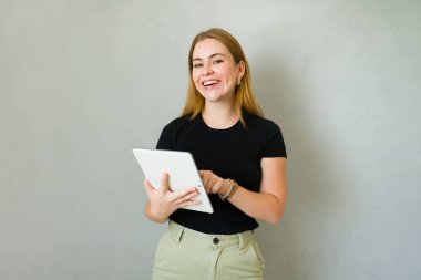 Güzel bir kadın, gri arka planı olan bir stüdyoda tablet bilgisayar kullanırken gülüyor.