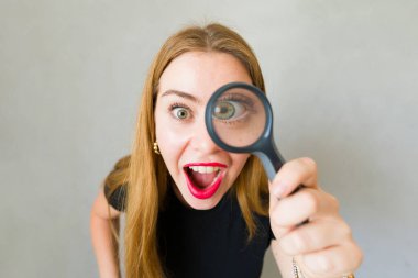 Heyecanlı kadın gözünün önünde bir büyüteç tutuyor ve ağzı açık bir şekilde ona bakıyor.