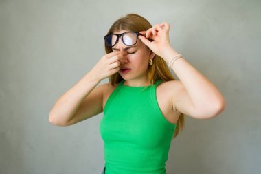 Genç kadın gözlüğünü çıkarıyor ve burnunun köprüsünü ovuyor, baş ağrısı var gibi görünüyor.