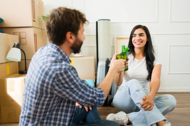 Genç çift yeni dairelerinde kutuları açmaya ara verirken bira şişeleriyle kadeh kaldırıyor.