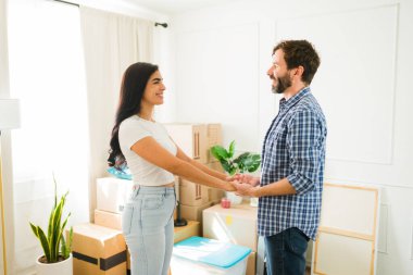 Yeni evlerinin oturma odasında el ele tutuşan ve birbirlerine bakan bir çiftin profil görüntüsü. Taşınmayı kutluyorlar.