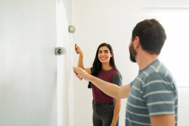 Neşeli çift gülümsüyor ve yeni evlerinin duvarlarını boyayarak eğleniyor.