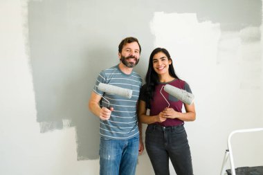 Şirin İspanyol çift ellerinde boya ruloları tutuyorlar ve yeni evlerinin duvarlarını boyarken gülümsüyorlar.