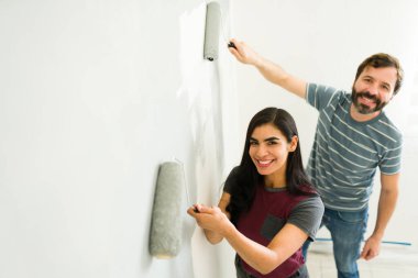 Genç İspanyol çift gülümsüyor ve yeni evlerinin duvarlarını boyarken eğleniyorlar.