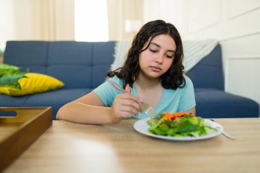Evde sağlıklı bir salata yiyen, yeme bozukluğu ve sağlık sorunlarıyla boğuşan, diyet ve akıl sağlığı arasındaki bağlantıyı vurgulayan isteksiz genç kız.
