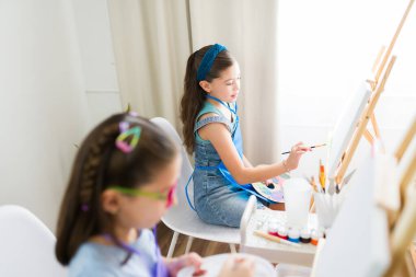 Sanat dersinde eğlenen iki genç kız, küçük tuvallerde resim yapıyorlar ve yeni sanatsal beceriler keşfediyorlar.