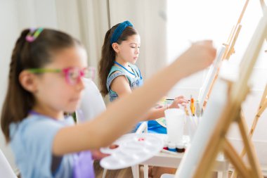 İlkokulda resim yaparken resim yapan iki genç kız.