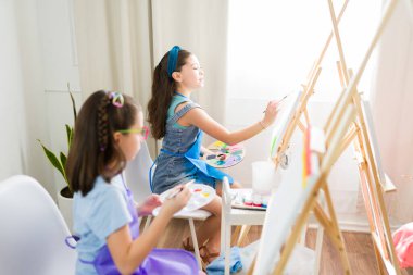 Güzel genç kızlar bir okul sanat dersi sırasında küçük tuvallere odaklanarak yaratıcılıklarını ve sanatsal becerilerini geliştiriyorlar.