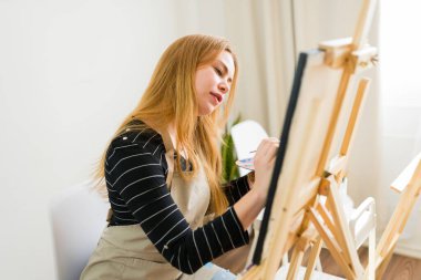 Sanat atölyesinde resim yapan kadın sanatçı palet ve fırçayla tuval üzerine resim yapıyor.