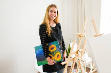 Sanat atölyesinde elinde bir ayçiçeği tablosu tutan neşeli bir sanatçının portresi, daha fazla sanat eseri yaratmaya hazır.