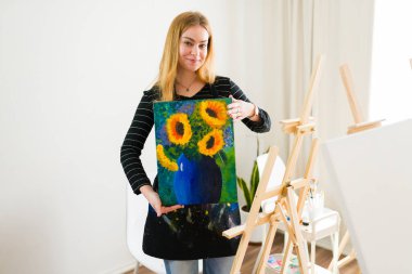 Sanat öğretmeni, bir ders sırasında öğrencilerine mavi bir vazoda tamamlanmış ayçiçeği resmini sunar.