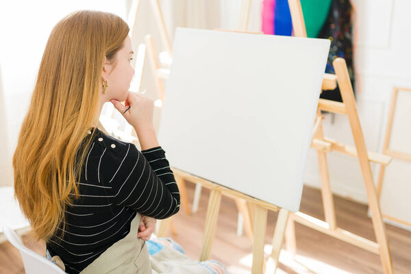 Творческая художница думает о своей следующей работе, глядя на чистый холст в своей художественной студии