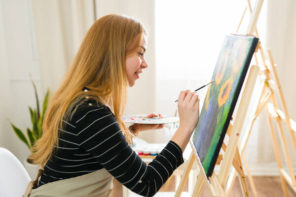 Female artist creating a vibrant and inspiring still life artwork by painting sunflowers on a canvas in her bright art studio